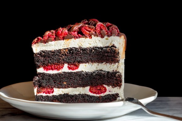 Chocolate raspberry layer cake slice on a plate. Side view. Close up. Black background